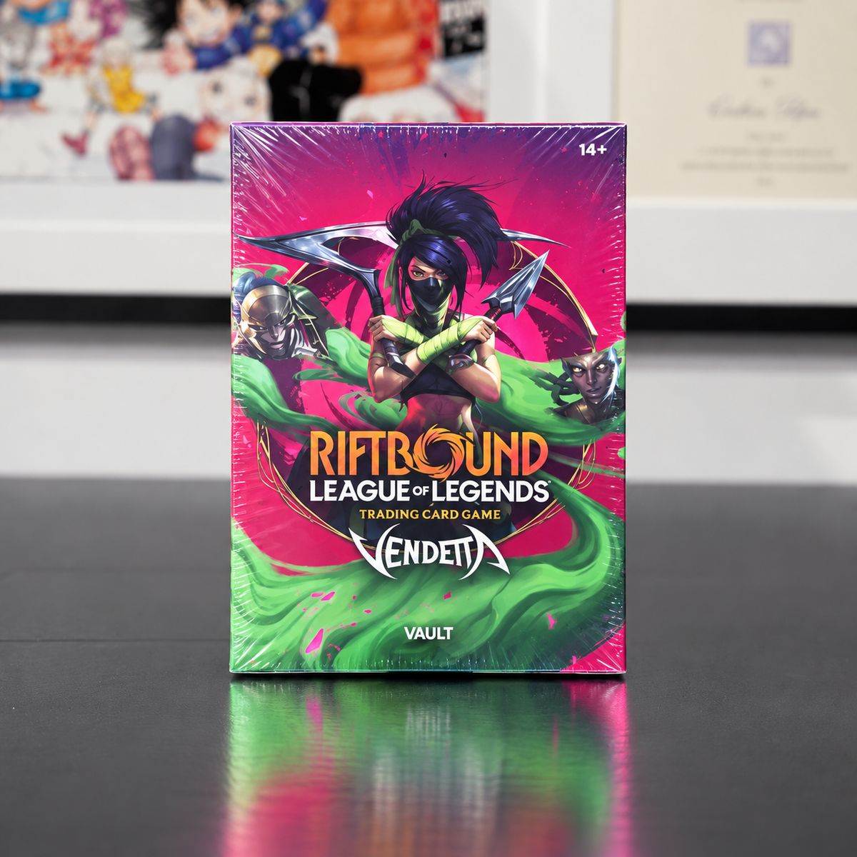 A boxed card game product standing upright on a dark reflective surface. The box is wrapped in clear plastic and features League of Legends Riftbound card game artwork with a pink and green color scheme and the Vendetta logo.